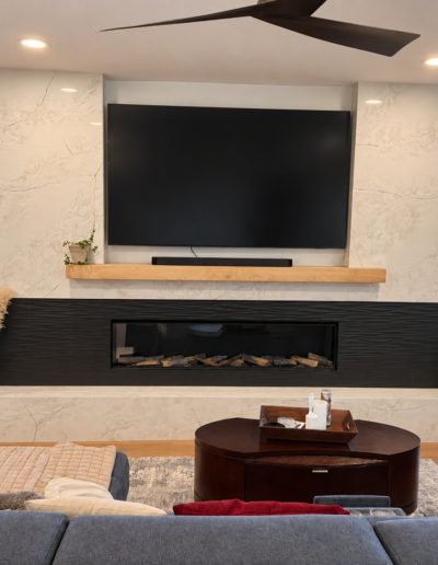 Completed living room remodel featuring a custom floor-to-ceiling fireplace with marble-look tile, black tile accents and a floating wood mantel