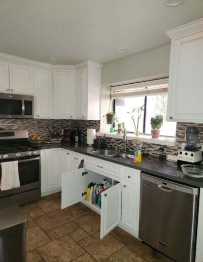 Existing kitchen sink and dishwasher area with white cabinets and dark countertops before conversion into a dining room in Cameron Park.