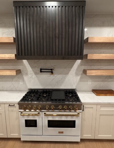 Completed kitchen remodel featuring a custom black range hood, floating wood shelves, full-height stone-look backsplash and professional-style range