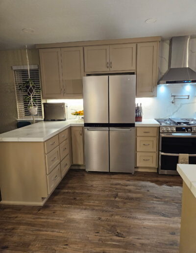New kitchen cabinetry and stainless steel refrigerator in Cameron Park with white quartz-look countertops, under-cabinet lighting and wood-look flooring.