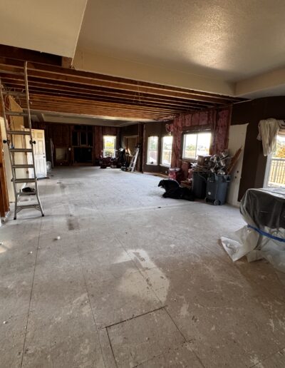 Kitchen and living room demolition in progress with exposed ceiling joists and removed flooring during open-concept renovation