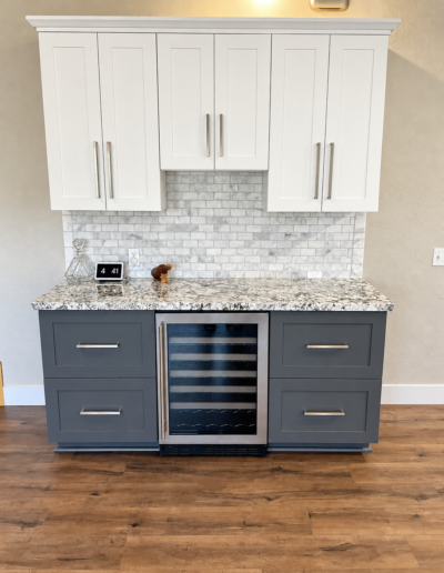 Custom built-in wine refrigerator with white shaker upper cabinets, gray base cabinets and granite countertop